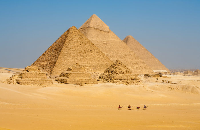 Row of Camels Walking at Great Egyptian Pyramids in Giza, Egypt A distant view of a row of tourist camels walking in front of all of the Egyptian Giza Pyramids together in Cairo, Egypt. Horizontal copy space